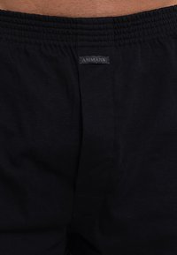 Zwarte katoenen shorts met een elastische tailleband, voorzien van een logotag "AMMANN" op de achterkant. Glad textuur en eenvoudig ontwerp.