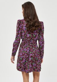Blumenkleid mit langen Ärmeln und gerafftem Bund. Dunkelviolette Hintergrund mit grünen und pinken Blumen. Glatter Stofftextur.