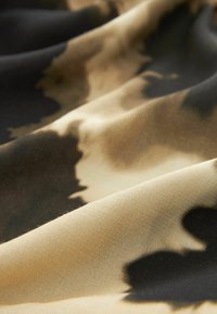 Blødt stof med et tan- og sort abstrakt mønster, der har en glat tekstur og en flydende drape, hvilket muliggør varieret anvendelse i design.
