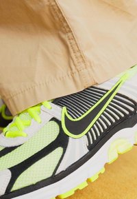 Nike sportiniai batai su pilku ir juodu tinkliuotu paviršiumi, neoninėmis geltonomis akcentais, tekstūruotu padu ir išskirtiniu swoosh logotipu.