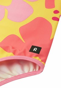 Badebekleidung mit einem bunten Muster aus rosa und gelben abstrakten Formen, mit einem rosa Saum und einem schwarzen Logoetikett am Rand.