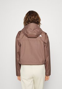 Bruine waterdichte jas met een capuchon, met een cropped ontwerp. De achterkant bevat een logo en heeft een gladde textuur, geschikt voor buitensport.