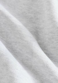 Tissu en coton blanc doux avec une texture fine tricotée et des plis doux créant une surface lisse et fluide.