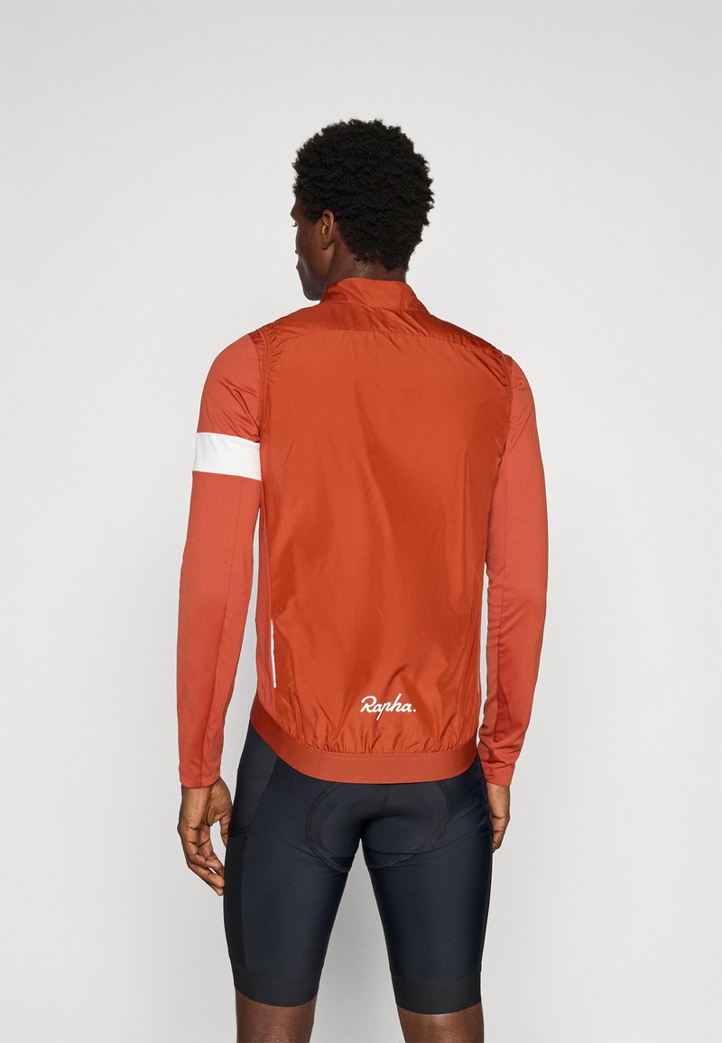 Rote Fahrradjacke mit langen Ärmeln, elastischen Bündchen und einem weißen Streifen am linken Arm. Glattes Material mit tailliertem Design. Markenlogo sichtbar.