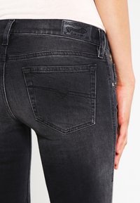 Black denim jeans featuring a fitted design, contrasting stitching, a rectangular back pocket, and a branded leather patch at the waist.
