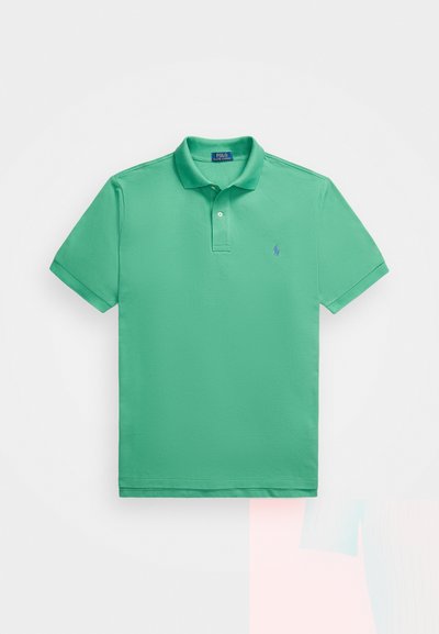 Grønn polo skjorte laget av myk bomull med korte ermer, klassisk krage og en liten blå logo på venstre bryst. Teksturerte stoffoverflater.