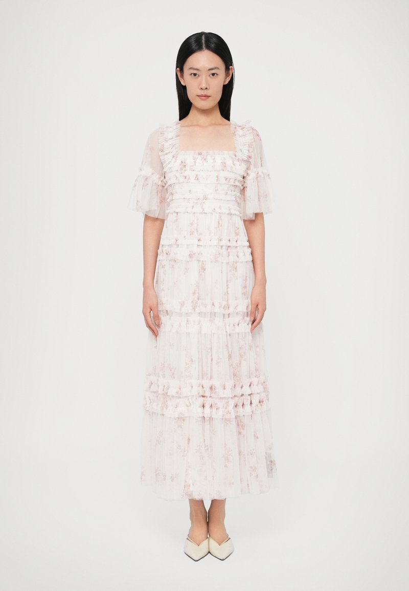 Długa, zwiewna sukienka z przeźroczystej jasnoróżowej tkaniny z kwiatowymi wzorami. Falbaniaste rękawy i warstwowy fason dodają faktury. Kwadratowy dekolt.