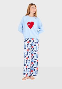 Sudadera azul clara con un gráfico de corazón rojo, combinada con pantalones de corte holgado que presentan un patrón abstracto multicolor en azul, rojo y blanco.