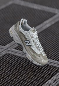 Tenisky New Balance v svetlo šedej a béžovej sieťovine s gumovými akcentmi, majú výrazné čierne logo 'N' a textúrovanú podrážku.