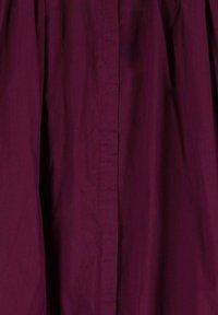 Tissu bordeaux avec une texture lisse, présentant une couture verticale au centre. Le matériau semble léger et légèrement respirant.