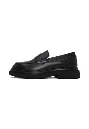 Mocasín negro de piel tipo slip-on con suela gruesa y tira decorativa en la parte superior, mostrado de lado sobre fondo blanco.