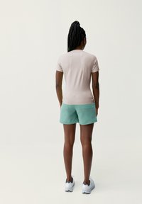 Svetlo béžový krátky rukávový top a mätovo zelené šortky, vyrobené z hladkej látky. Biele športové topánky s šedými akcentmi. Minimalistický dizajn.