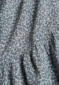 Tissu bleu avec petit imprimé floral blanc et détail de couture froncée créant de doux plis et une texture.