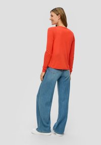 Maglione rosso a maniche lunghe abbinato a jeans a gamba larga blu chiaro e sneakers bianche. Il maglione presenta un collo rotondo e maniche aderenti.