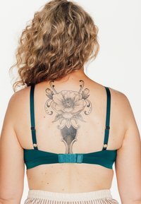 Soutien-gorge in tessuto teal con spalline regolabili, texture liscia e chiusura con gancio e occhiello. Il retro presenta un design di tatuaggio floreale.