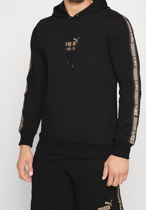 Mand iført sort Puma hættetrøje og shorts med gul tekst "KING" på ærmerne og logo på brystet og venstre ben.