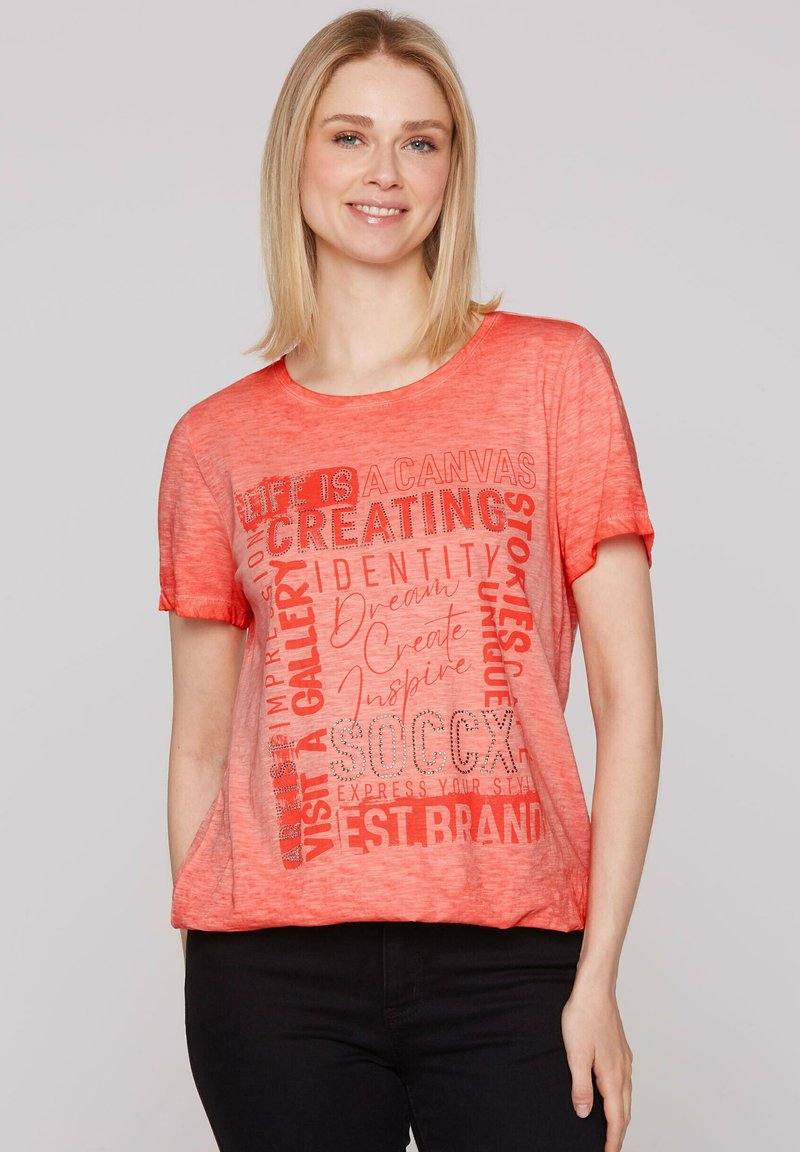 Camiseta de manga corta en color coral con tipografía mixta y elementos gráficos en un tono más claro. Tejido suave y texturizado. Corte casual.