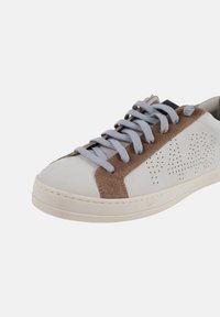Zapatilla blanca con acentos de ante marrón, lengüeta acolchada y cordones grises. Diseño lateral perforado y suela de goma para mayor tracción.