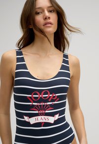 Marine gestreept badpak met witte strepen en een opvallend rood logo met "JOOP!" en "JEANS" op de voorkant. Soepele, rekbare stof.