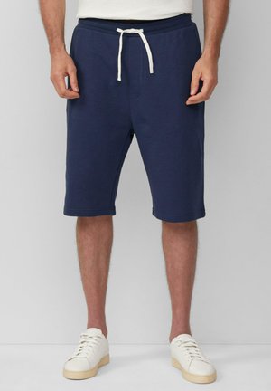 Navyblauwe knielange shorts van zacht materiaal met een trekkoord in de taille en voorzakken, gecombineerd met witte sneakers.