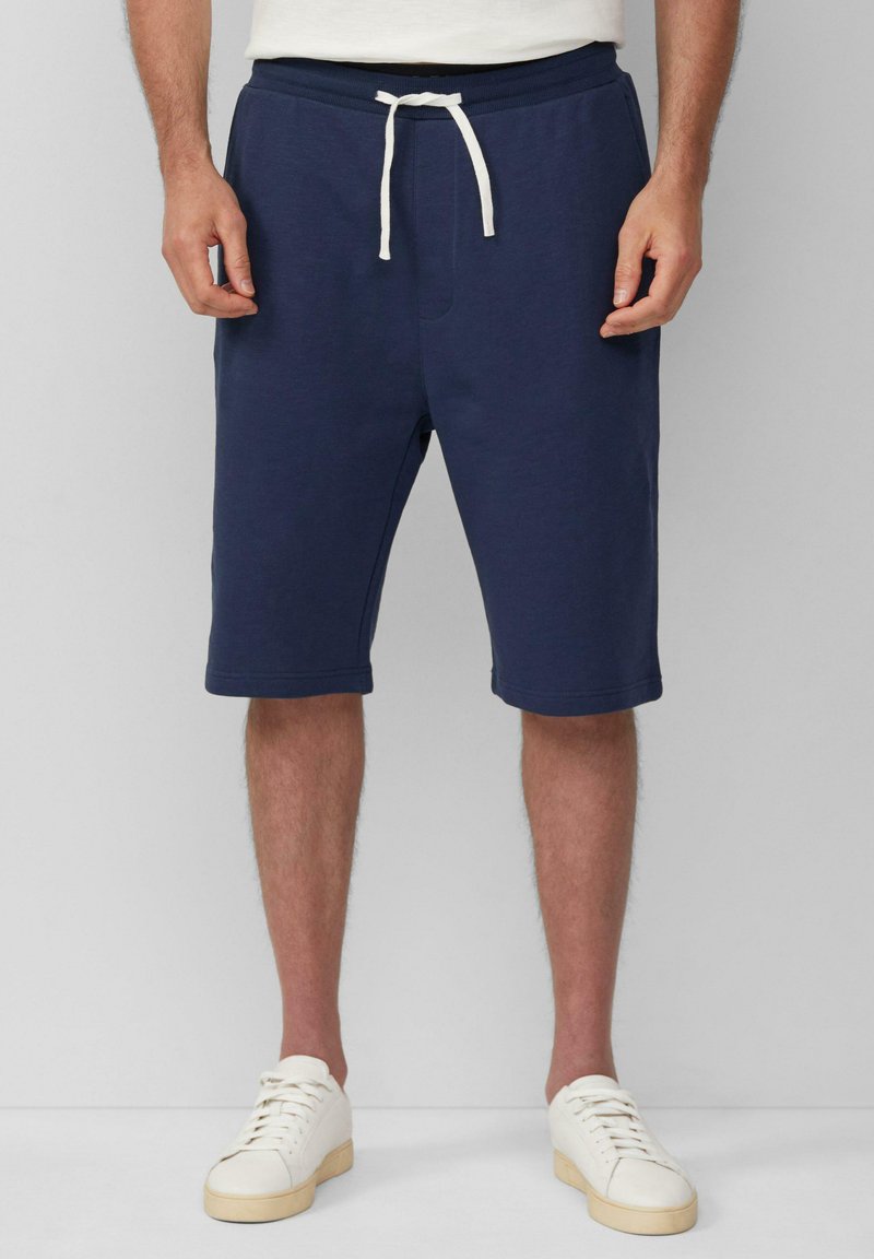 Navyblauwe knielange shorts van zacht materiaal met een trekkoord in de taille en voorzakken, gecombineerd met witte sneakers.