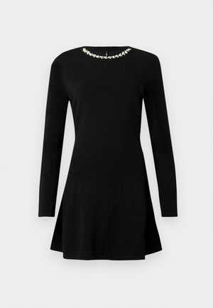 Rochie neagră cu mâneci lungi, ajustată, cu o ușoară fustă la tiv și ornamente florale decorative albe în jurul decolteului.