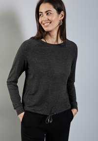 Suéter gris oscuro con una sutil textura moteada, mangas raglán y un escote redondeado. Presenta un cordón funcional en el dobladillo.