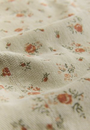 Világos bézs színű szövet, amely tompa piros és zöld virágmintával rendelkezik. Texturált felület látható vászonos szövésmintával és szórványosan elhelyezkedő apró virágokkal.