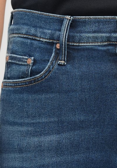 Close-up van de taille van blauwe denim jeans met zichtbare riemlus, voorzak en een deel van een zwarte top.