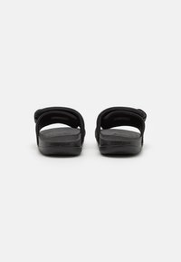 Black sandals with two wide straps, a textured footbed, and a contoured sole, showcasing rubber material and minimalistic design.