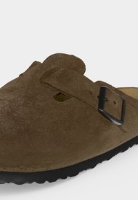 Καφέ παπούτσι από σουέντ slip-on με μαύρο ρυθμιζόμενο λουράκι με αγκράφα και υφασμένο μαύρο πέλμα.