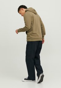 Felpa verde oliva con tasca a marsupio, abbinata a pantaloni cargo blu navy. L'outfit presenta polsini a coste e sneakers nere.