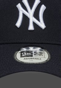 Tengerészeti baseball sapka fehér hímzett New York Yankees logóval. Anyaga struktúrált szövet, kör alakú címkével, ami a "New Era Adjustable" feliratot viseli.