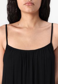 Černý bezrukávový top s tenkými ramínky, s texturovaným, skládáním designem a volným střihem, který zvýrazňuje výstřih a ramena.