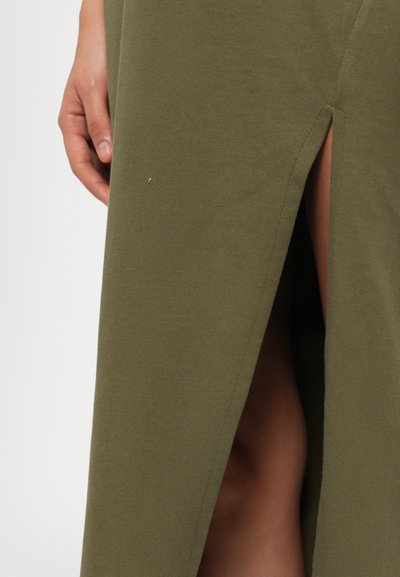 Olive green skirt made of soft fabric, featuring a side slit and smooth texture. Visible hand holding the fabric at the slit.