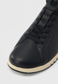 Gros plan sur l'avant d'une chaussure de sport en cuir noir avec des lacets noirs et une semelle en caoutchouc blanche sur fond clair.