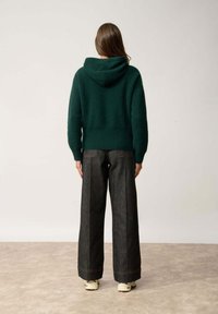 Zielona, teksturowana dzianinowa bluza z kapturem z szwem na plecach; w połączeniu z szerokimi, ciemnoniebieskimi dżinsami z kontrastowymi przeszyciami i wyraźnymi kieszeniami.