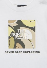 Άσπρο ύφασμα με πολύχρωμο αφηρημένο τετράγωνο που περιέχει το λογότυπο The North Face και το κείμενο «NEVER STOP EXPLORING» από κάτω.