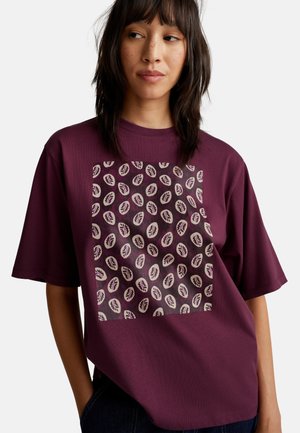 Vínově červené oversized tričko s krátkými rukávy a čtvercovým grafickým vzorem se listy na tmavém pozadí. Měkký bavlněný materiál.