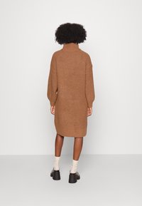 Abito maglione marrone in maglia con collo alto, maniche lunghe e vestibilità rilassata, che arriva a metà coscia; tessuto testurizzato e orlo a coste.