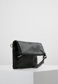 Czarna skórzana torba na ramię z klapką na złożenie, srebrnym okuciem, teksturowaną powierzchnią i regulowanym paskiem.