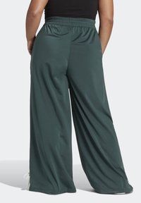 Široké kalhoty z tmavě zelené látky s hladkým povrchem, s elastickým pasem a nastavitelnými vázáním na lemech.