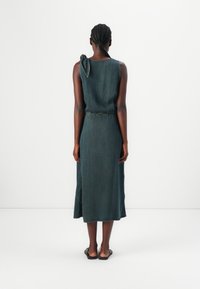 Green denim dress with a sleeveless design, tie detail on one shoulder, and a mid-calf length. Smooth texture and simple silhouette.