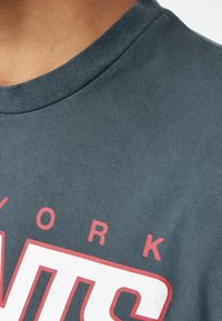 Harmaa puuvillapaita, jossa on pyöreä kaula-aukko, ja jossa on punaisella graafisella tekstillä lukee "NEW YORK" ja "PANTS" lihavoidusti. Sileä pinta, rento muotoilu.