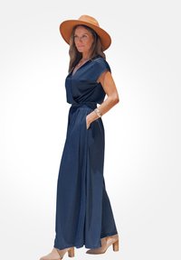 Mono azul marino de mangas cortas, con cintura entallada y bolsillos. Combinado con un sombrero de ala ancha color beige y zapatos de tacón cuadrado beige.
