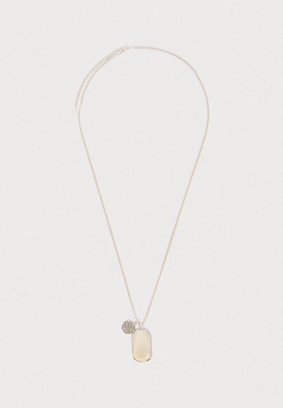 Stříbrný řetízek se dvěma přívěsky: hladký obdélníkový štítek a malý kulatý disk se šachovnicovým vzorem.