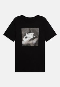 Juodas medvilninis marškinėliai su apvaliu kaklu, ant priekinės pusės vaizduojant sidabrinę atspindinčią Nike logotipą kvadrato grafiko viduje.