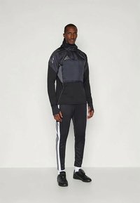 Conjunto atlético masculino com uma jaqueta preta com capuz e detalhes cinzentos, combinado com calças pretas que apresentam riscas brancas nas laterais.