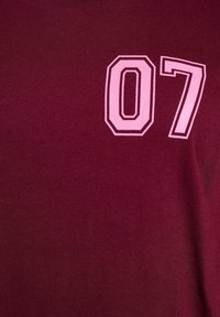 Burgundské tričko s jemnou textúrou, na prednej strane s veľkým ružovým číslom "07" vytlačeným tučným písmom.