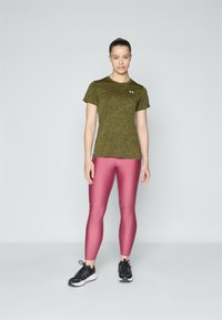 Grønn heathered treningstrøye med korte ermer, paret med glitrende rosa leggings. Svarte treningesko med strukturerte såler.